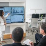 woman in white suit discussing stock market data to her colleagues