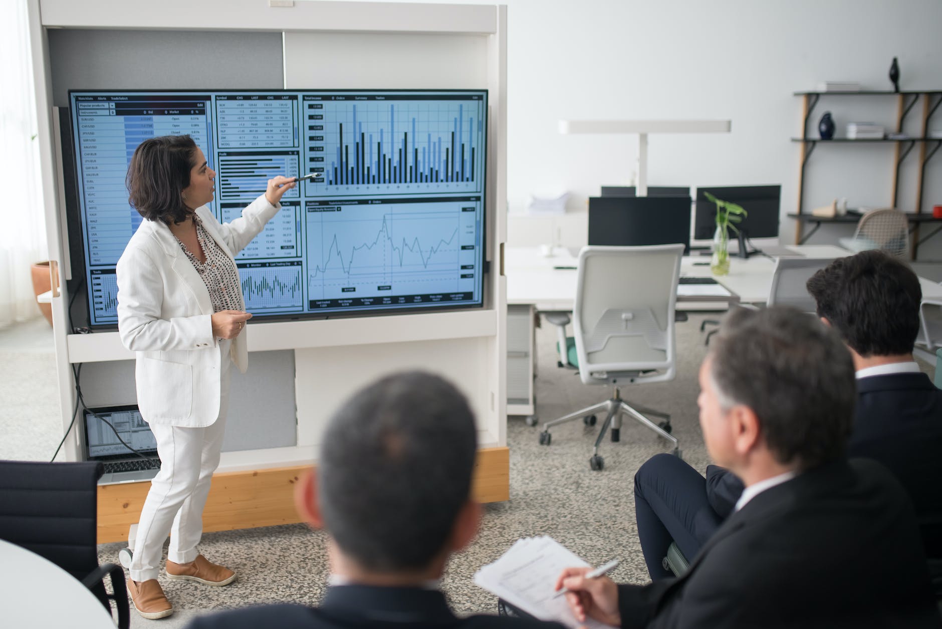 woman in white suit discussing stock market data to her colleagues