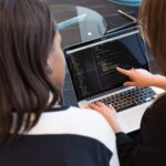 two women looking at the code at laptop