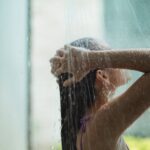 anonymous young woman washing hair under shower