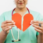 woman in teal scrub shirt holding heart shaped red paper