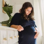 smiling pregnant woman caressing tummy in house room